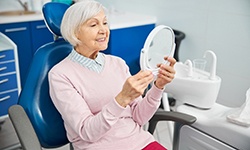 Senior woman sitting in dental chair checking smile in mirror