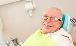 Senior man with glasses sitting in dental chair smiling