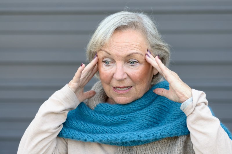 Older woman with gum disease in Frisco holding her head.