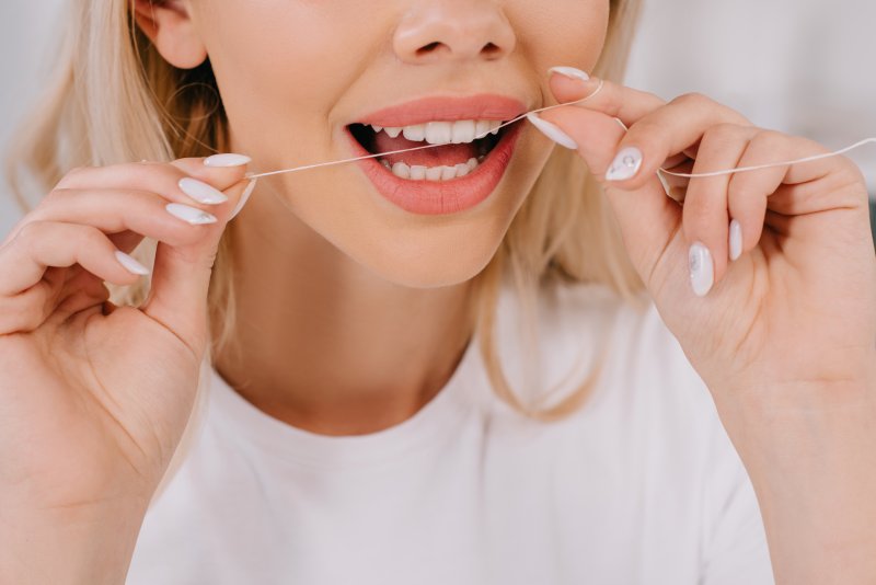 Woman with gingivitis in Frisco flossing her teeth