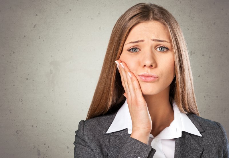 Woman with gum disease in Frisco holding her face