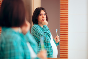 Concerned pregnant woman with gum disease looking in a mirror